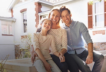 Parents and child sitting in front of home smiling.