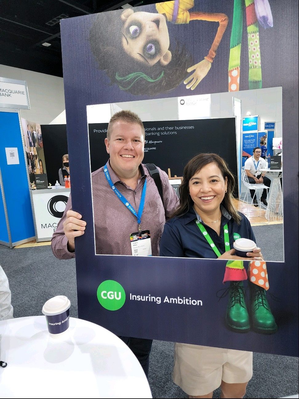 Two people having a coffee while behind the tall poppy board