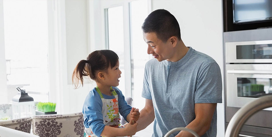 Two people in kitchen, younger person with apron talking to adult.